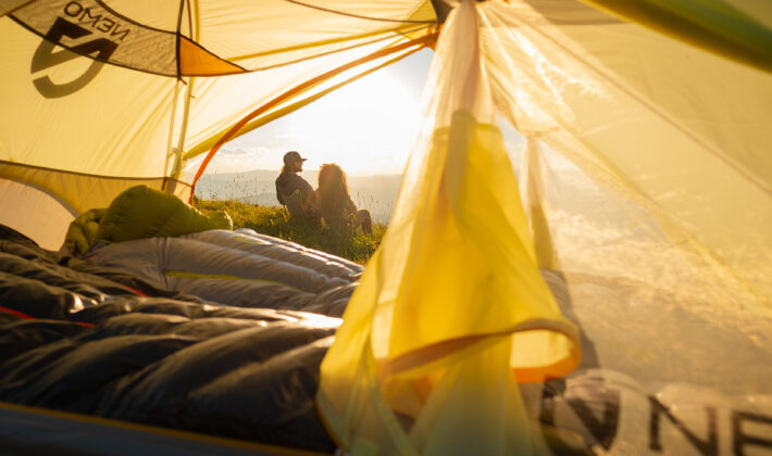 photo from inside of a tent showing two people sitting outside the tent